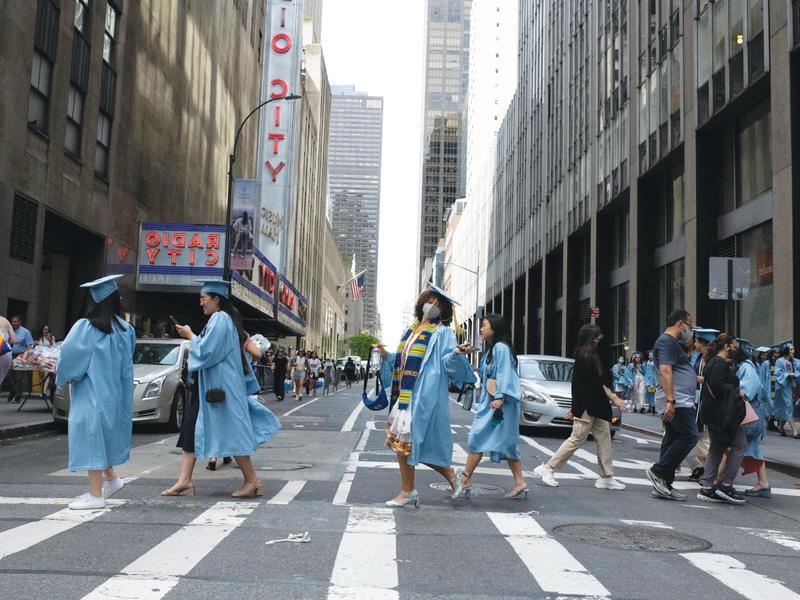 身着毕业礼服的十大电竞游戏综合排名女学生大步走过城市人行横道